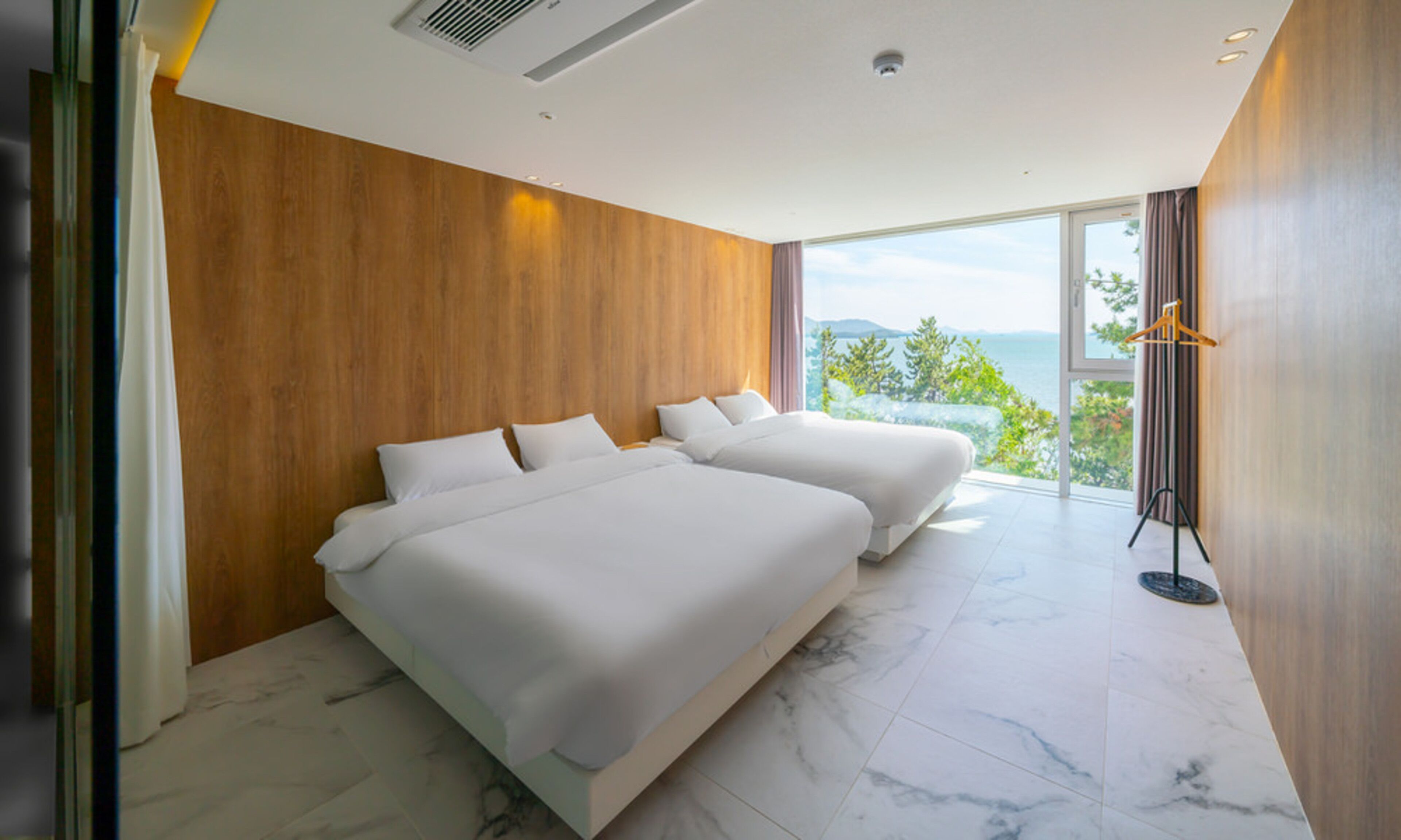 Ein modernes Hotelzimmer mit zwei Betten, einem großen Fenster mit Meerblick und einer Wand mit Holzverkleidung.