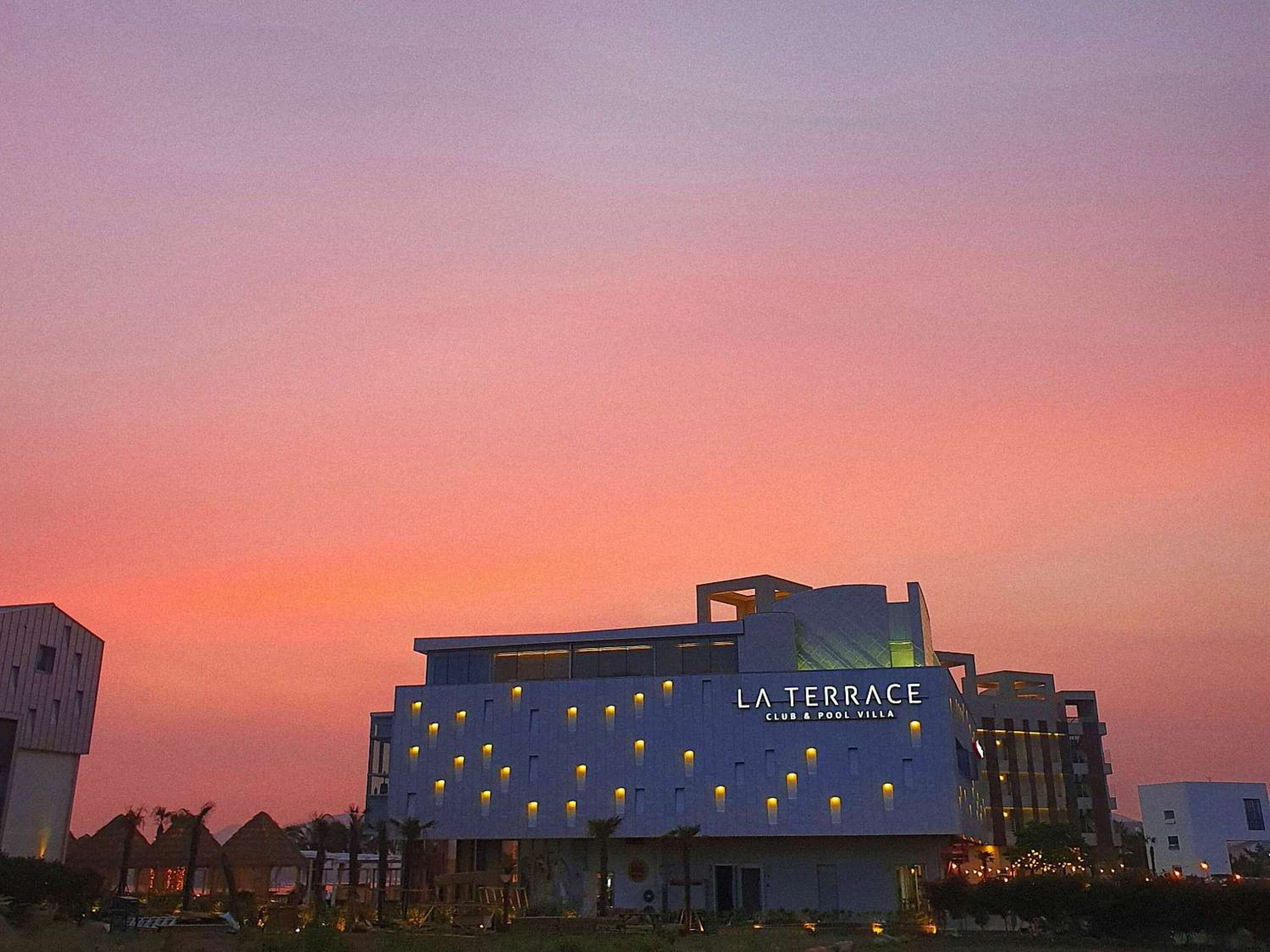 A modern building with the sign "LA TERRACE CLUB & POOL VILLA" at dusk.