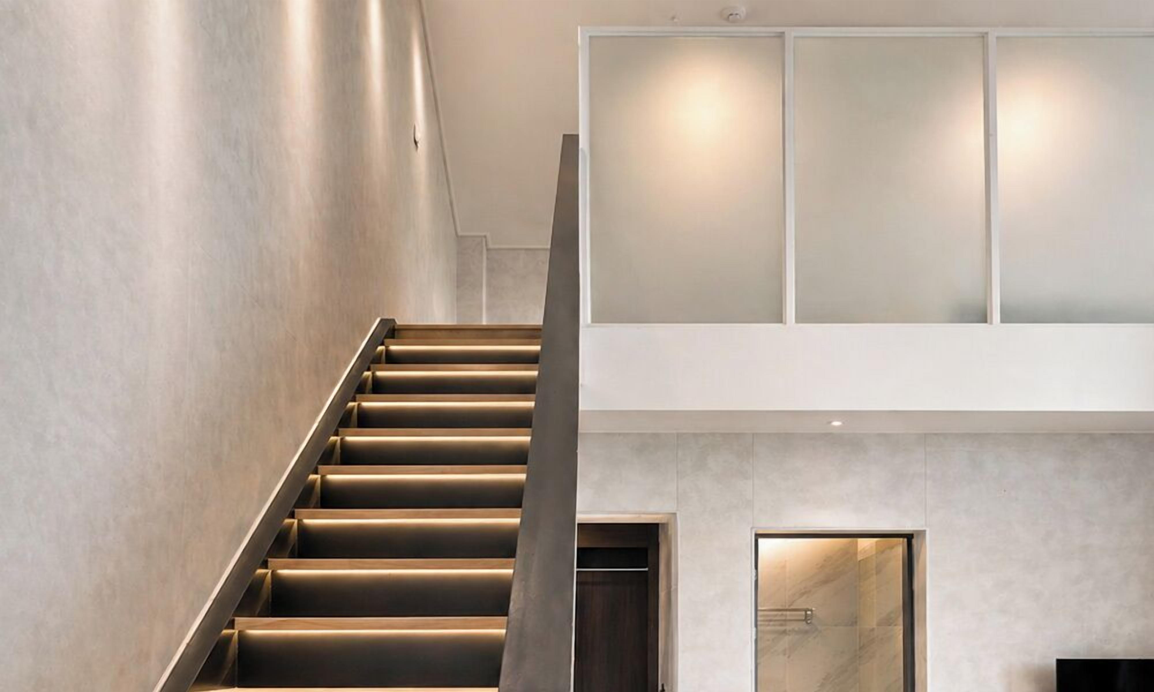 Een modern interieur met een trap naar een verdieping, een glazen deur en een wandlamp.