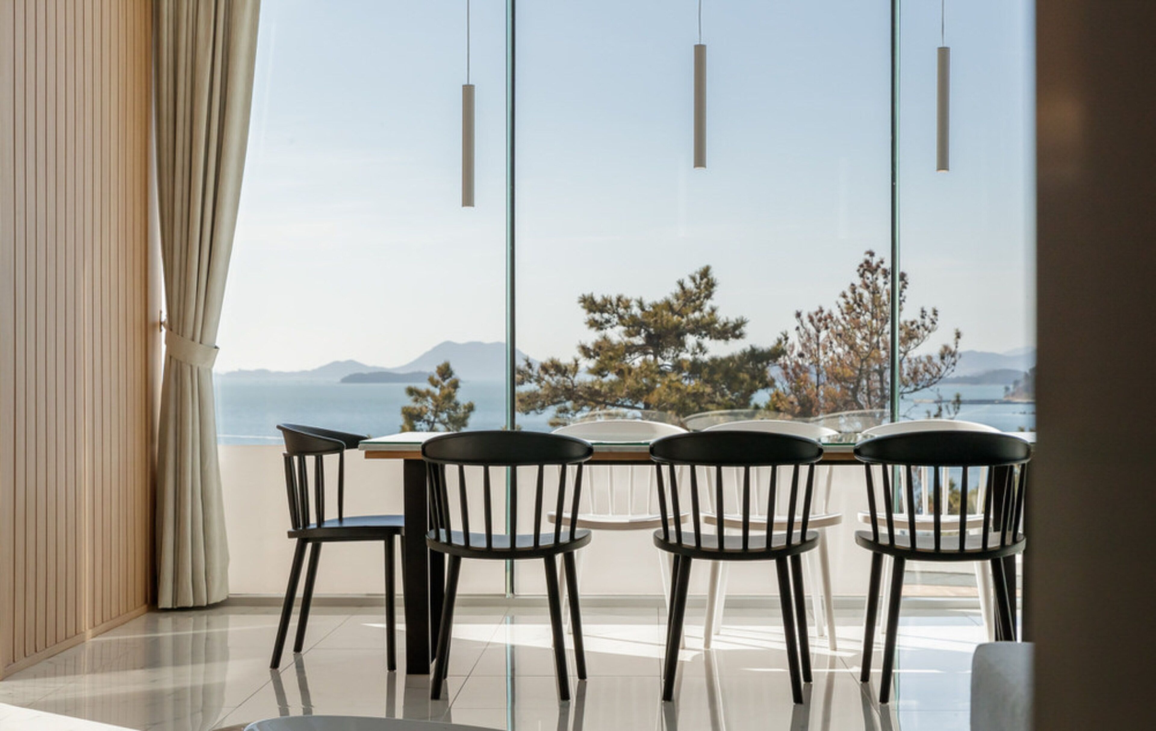 Ein moderner Essbereich mit Tisch und vier Stühlen, großen Fenstern mit Blick auf Bäume und Berge sowie Pendelleuchten.