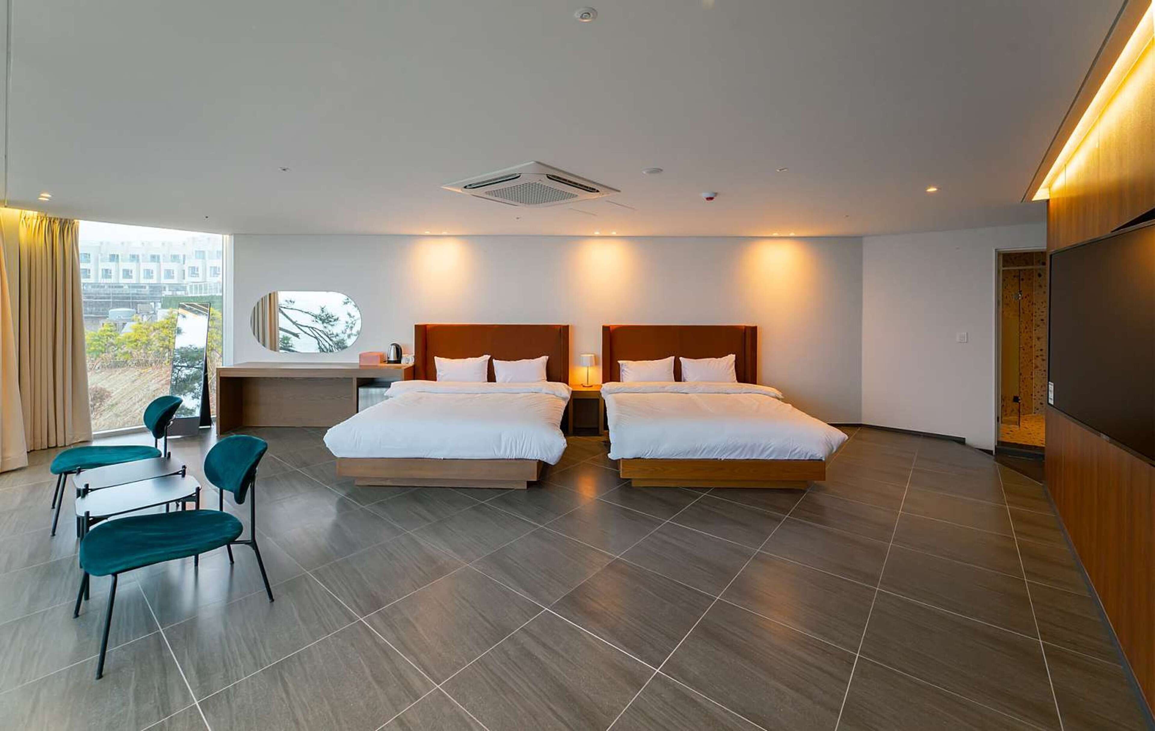 Una habitación de hotel moderna con dos camas, un escritorio, sillas y un ventanal con vistas.