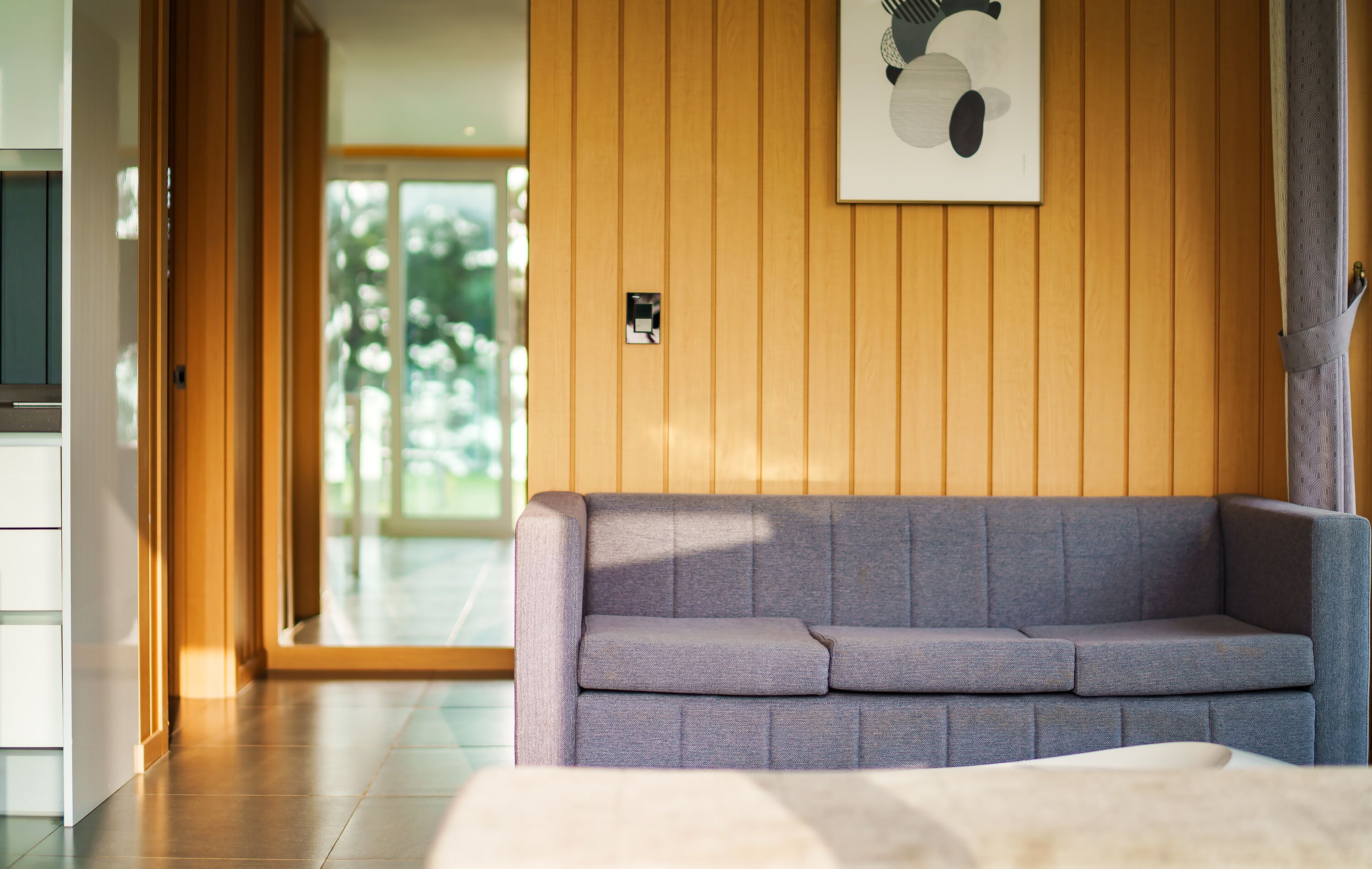 A modern living room with a grey sofa, wooden panel walls, and a framed artwork.