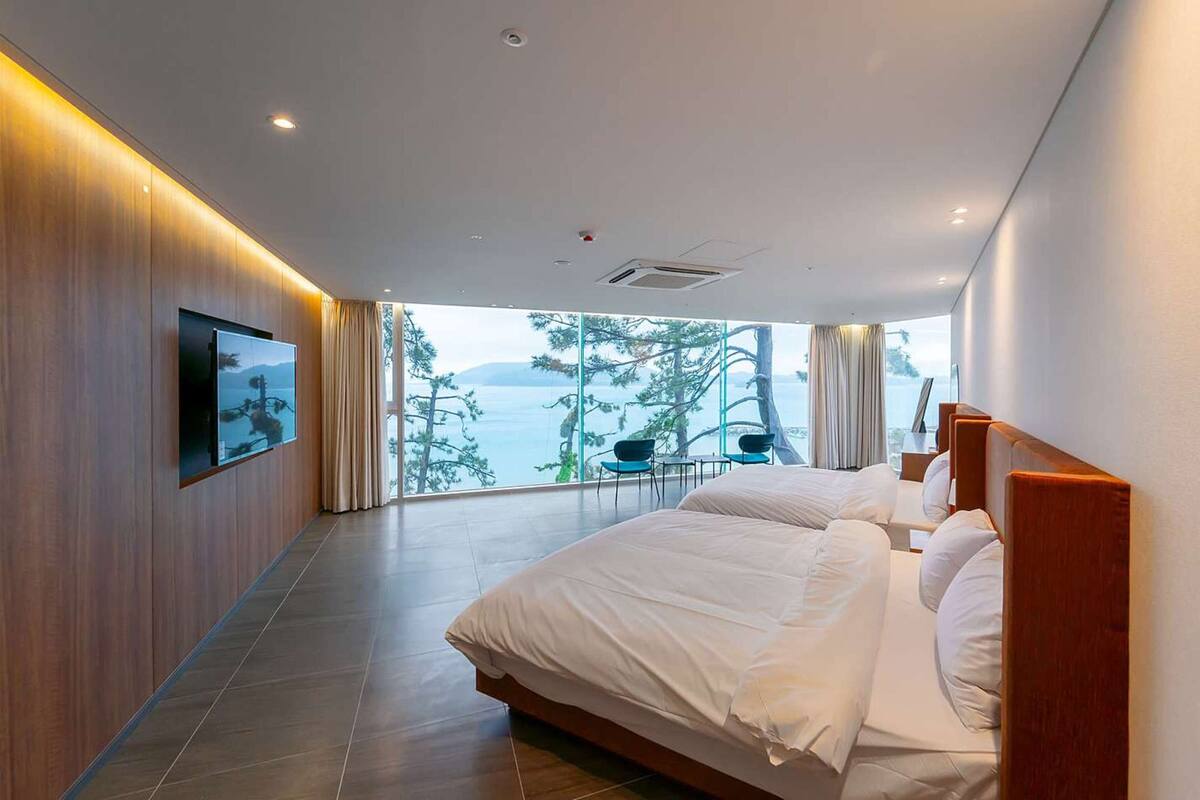 Ein modernes Hotelzimmer mit einem großen Bett, einem an der Wand montierten Fernseher und einem Balkon mit Blick auf Bäume und Wasser.