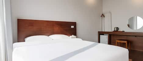 Une chambre d’hôtel moderne avec un grand lit, une tête de lit en bois, un bureau avec un miroir et un petit tabouret.