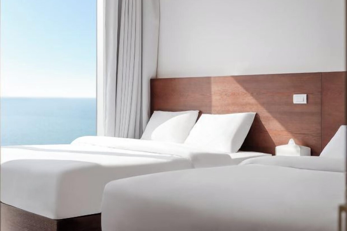 A hotel room with two beds, a wooden headboard, and a view of the sea.