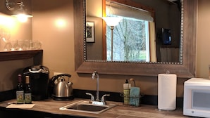 A hotel kitchenette with a sink, kettle, wine bottles, and a microwave.