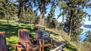 Outdoor wooden chairs arranged on a grassy area with a view of a lake and trees in the background.