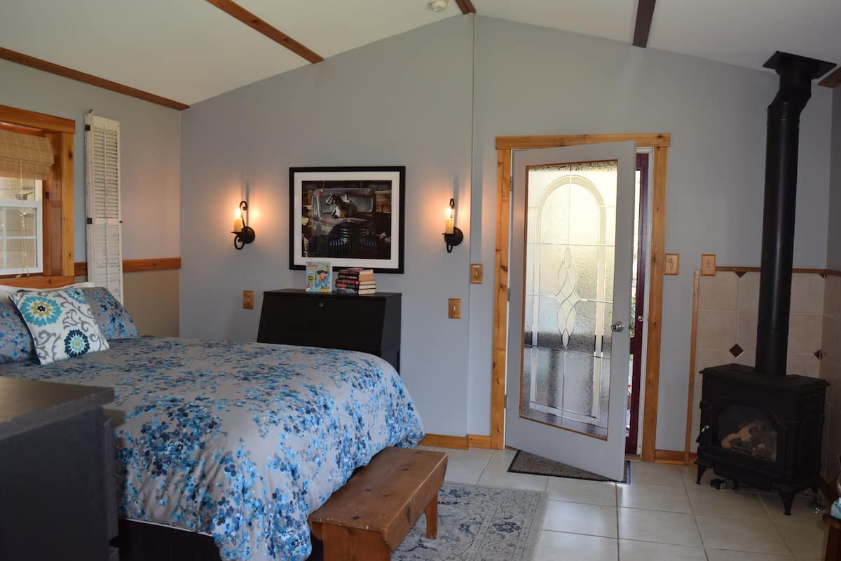 Een slaapkamer met een bed, een bankje, een open haard en een deur die uitkomt op een balkon.