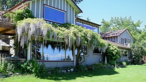 A two-story house with large windows, a covered porch, and lush greenery.