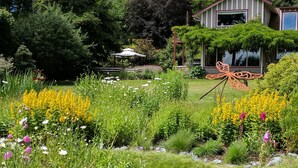 A garden with a variety of plants and flowers, a gazebo, and a house with a butterfly sculpture in the foreground.