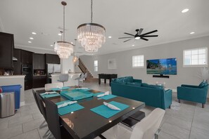 A modern kitchen with dark cabinets, a dining area with a black table and blue placemats, a teal sofa, and a ceiling fan.