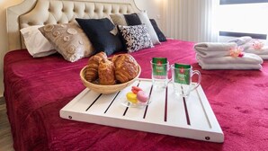 A neatly made bed with a red bedspread, a tray with croissants, macarons, and two glasses of water. - Studio between King David Hotel and Waldorf - Parking Included (Jerusalem)