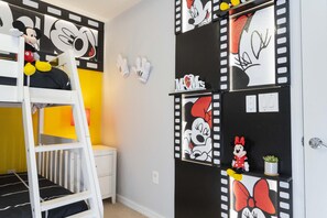 A child's bunk bed with Mickey Mouse decorations, a ladder, and a small nightstand.