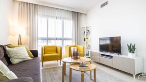 A modern living room with a sofa, two yellow armchairs, a coffee table, a TV, and a bookshelf. - Haneviim Court: 1BR Apartment in Jerusalem (Jerusalem)
