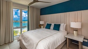 Habitación de hotel con una cama grande, dos lámparas de noche, un ventilador de techo y vista al mar.
