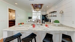 A modern kitchen with a marble island, bar stools, and a dining area.