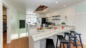 A modern kitchen with a marble countertop, stainless steel appliances, and a hanging light fixture.