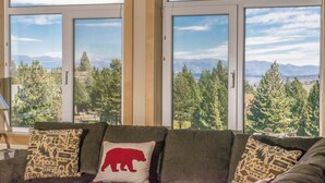 A living room with a sofa and cushions, large windows with a mountain view, and a wooden ceiling. - Ski-in Ski-Out Great Views Extra Large Living Room Top Floor Two Balconies (Mammoth Lakes)