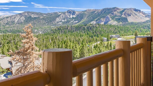 A mountain view from a balcony with wooden railings, a dry tree, and a forested valley. - Ski-in Ski-Out Great Views Extra Large Living Room Top Floor Two Balconies (Mammoth Lakes)