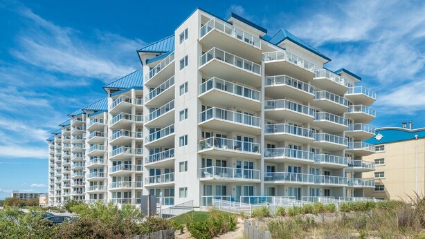 Un hotel de varios pisos con balcones, vista al mar y un estacionamiento.