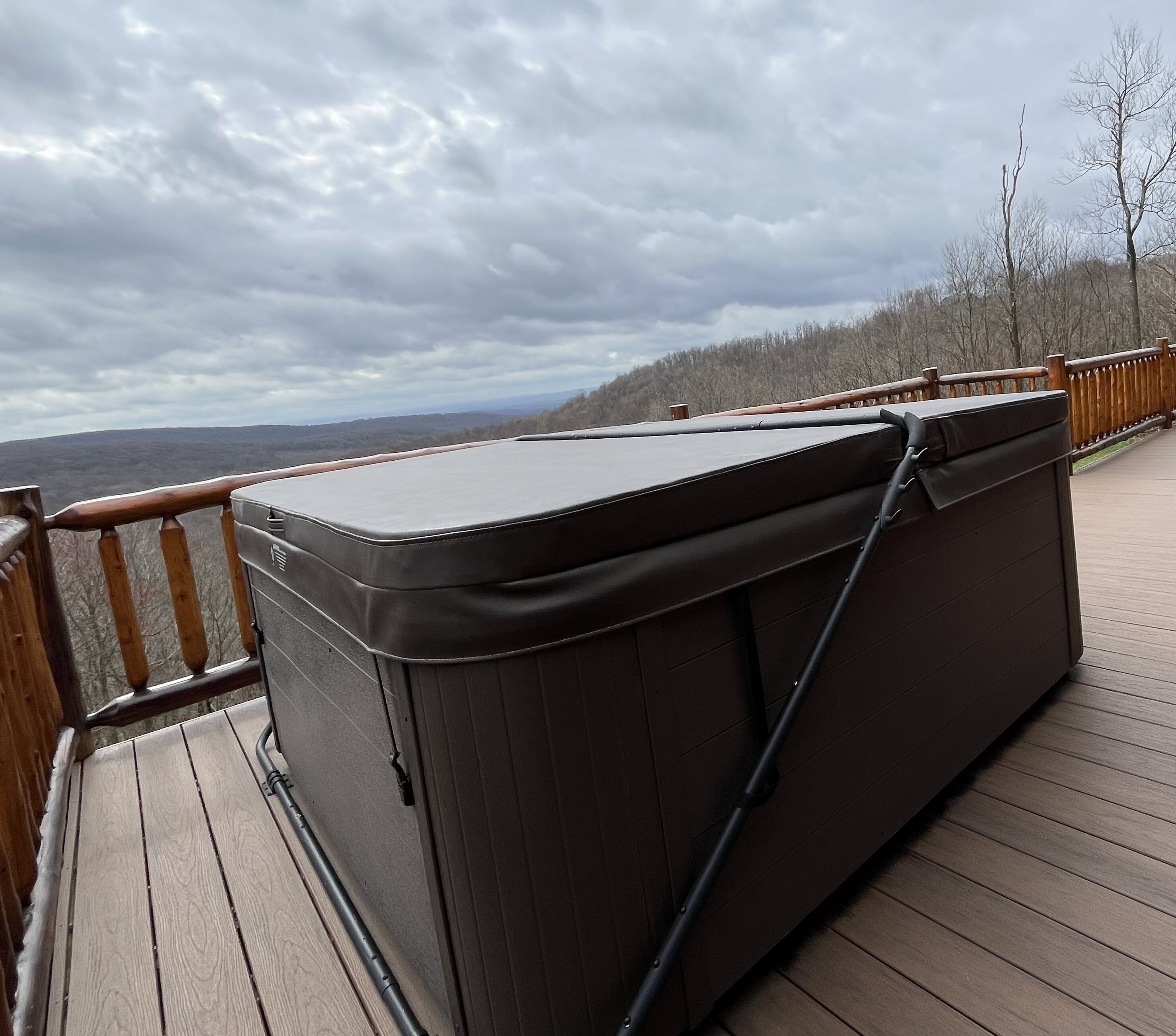 Ein Whirlpool auf einer Holzdiele mit Blick auf ein bewaldetes Gebiet und Hügel im Hintergrund.