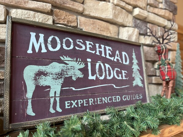 Ein Holzschild mit einem Elch und den Schriftzügen "Moosehead Lodge" und "Erfahrene Guides" vor einer Steinsäule.