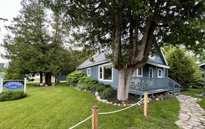 A house with a blue exterior, surrounded by a well-maintained lawn and a stone pathway leading to the entrance. - Spacious home in Omena. Dog friendly. Short walk to beach. (Omena)