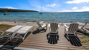Una terraza de madera con sillones de descanso frente a un lago tranquilo, barcos y una orilla lejana.