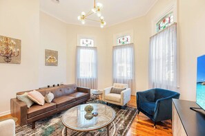 A living room with a brown sofa, a white armchair, a blue armchair, a glass coffee table, and a television. - Luxury on the Esplanade - Echuca Holiday Homes (Echuca)