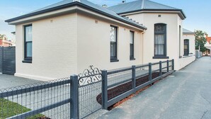 A two-story building with a beige exterior and black trim. It features a metal fence with decorative elements and a small garden area in front. - Luxury on the Esplanade - Echuca Holiday Homes (Echuca)