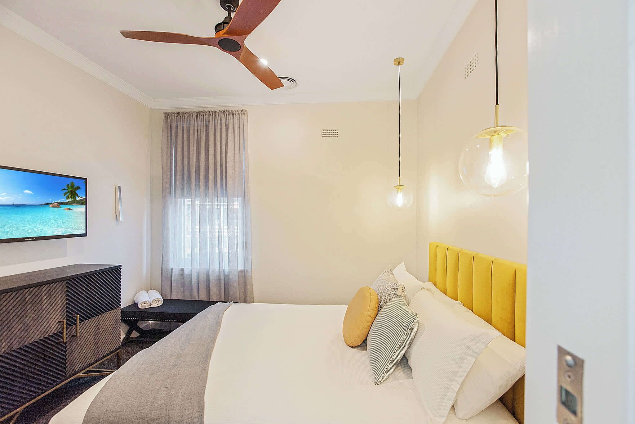 A modern hotel room with a bed, a TV, a ceiling fan, and a view of the ocean.