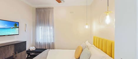 A modern hotel room with a bed, a TV, a ceiling fan, and a view of the ocean.