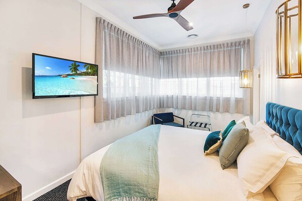 A hotel room with a bed, a desk, a chair, a television, and a ceiling fan.