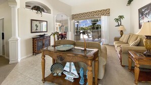 A spacious living room with a high ceiling, a ceiling fan, a dining area with a view, and a cozy seating area with a sofa and a lamp. - Casa Del Sol, full refund*, heated pool, sleeps 6 (Port Charlotte)