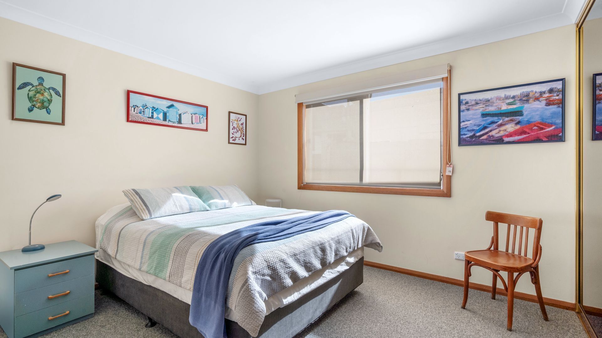 A bedroom with a bed, a desk, and a chair. There are paintings on the walls.