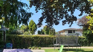 Un jardin avec une cabane de jeu rose, un trampoline et un toboggan vert.