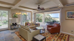 A spacious living room with a beige sofa, a brown leather chair, and a coffee table. There is a large window providing a view of the outdoors. - Wai'ula'ula: You Can't Beat This View  (Waimea)