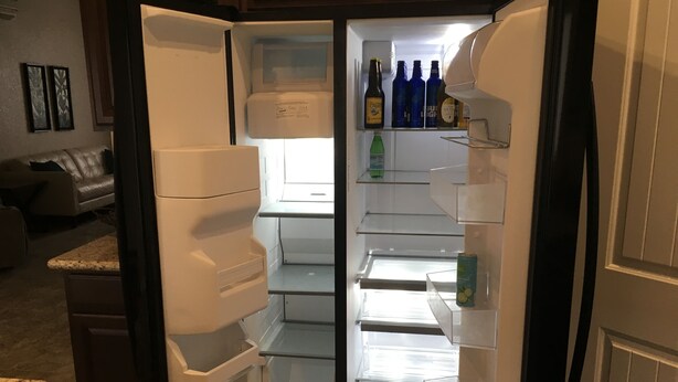 Ein offener Kühlschrank mit Regalen und einem Gefrierfach, der Getränke und eine Dose enthält.