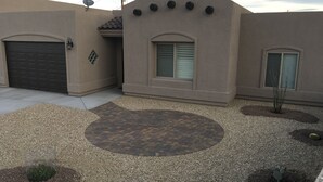 Ein Wohngebäude mit Garage, einer kleinen Terrasse mit kreisförmigem Mauerwerk und einigen Blumentöpfen.