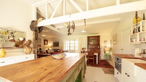 A kitchen with wooden countertops, a large island, hanging utensils, and a dining area with a table and chairs. - Stables Cottage; awaken to the sound of a river flowing over rapids. <br><br> (Frasertown)
