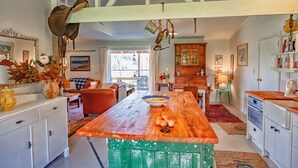 A kitchen with a wooden island, white cabinets, and a dining area with a red sofa and a table. - Stables Cottage; awaken to the sound of a river flowing over rapids. <br><br> (Frasertown)