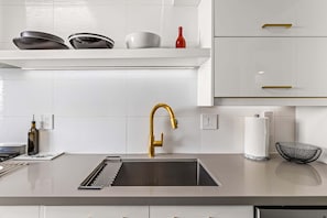 A modern kitchen with a stainless steel sink, gold faucet, white cabinets, and a black wire basket.