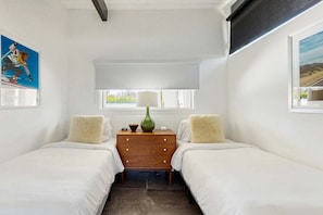 A bedroom with two beds, a wooden dresser, a lamp, and a window with a view.
