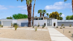 A modern house with a garage, palm trees, and a garden with various plants.