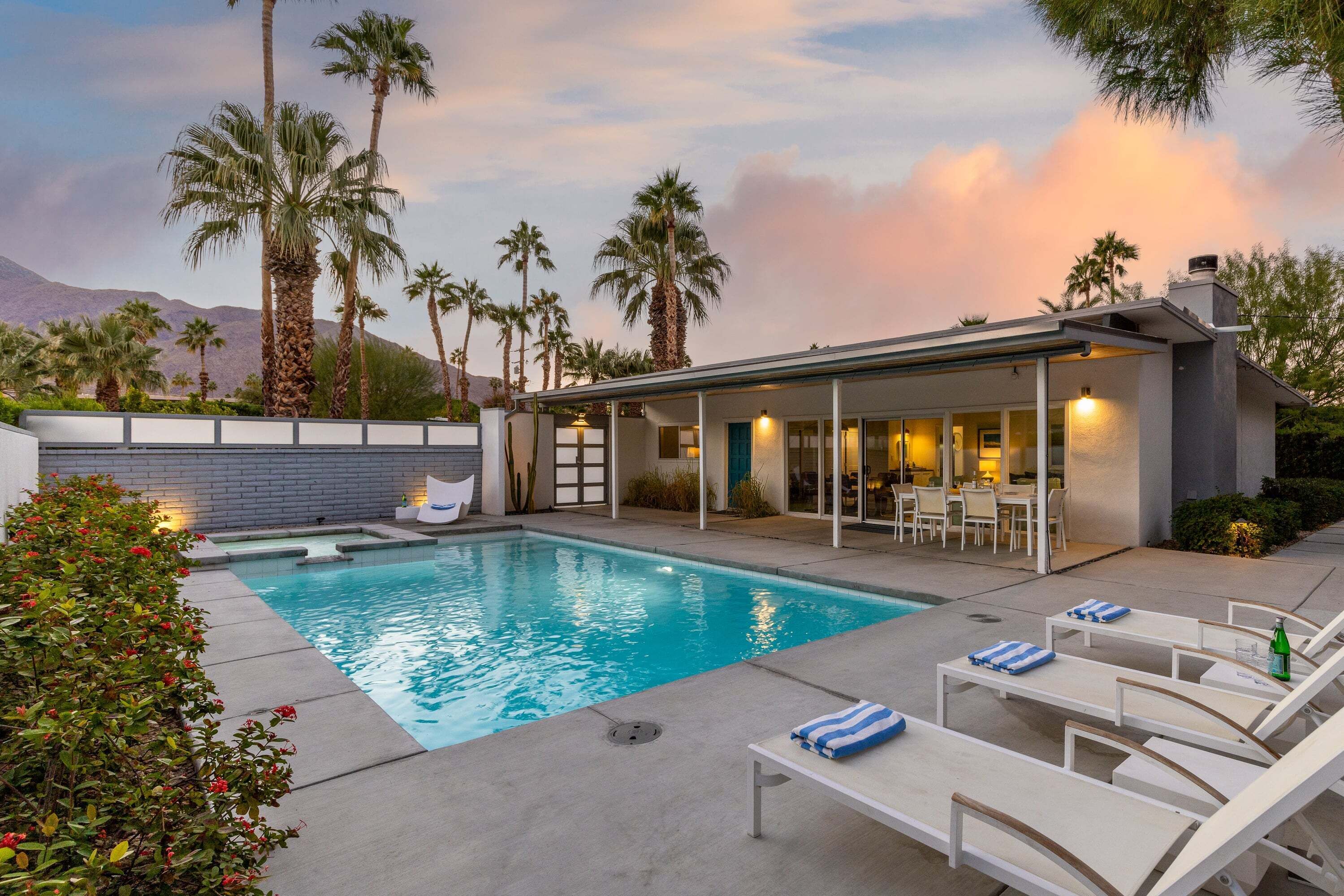 A swimming pool with lounge chairs, a covered patio, and palm trees.