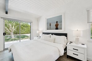 A modern bedroom with a large bed, a nightstand, a bedside table, and a framed picture on the wall.