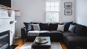 A modern living room with a black leather sofa, a wooden coffee table, and a white brick fireplace. - The Station Master's House, A darling house with everything you need for a relaxing getaway in Castl... (Castlemaine)