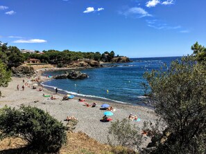 Une plage où l’on peut se détendre au soleil et se baigner, entourée d’un paysage rocheux et de quelques arbres.