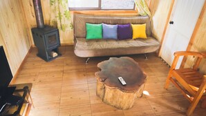 A cozy cabin interior with a wooden floor, a sofa with colorful cushions, a small table, and a wood-burning stove.