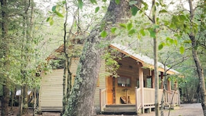 A rustic cabin with a wooden porch, surrounded by trees.
